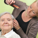 Caregiver grooming elderly woman